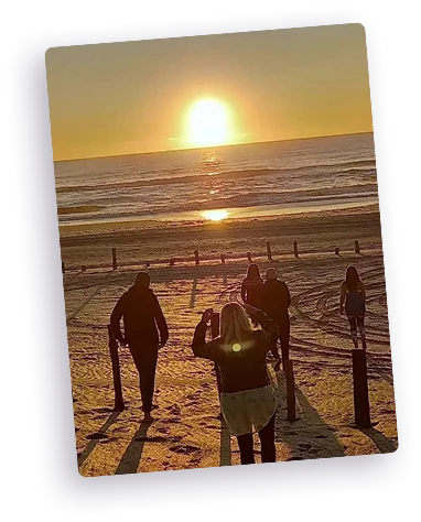 Grupo de personas en silueta en una playa al atardecer, con el sol reflejándose en el mar.