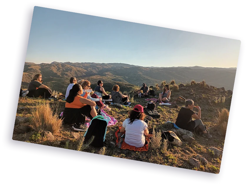 Grupo de personas sentadas en una colina disfrutando de un picnic al aire libre con montañas de fondo al atardecer.