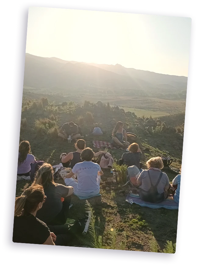 Grupo de personas sentadas en un cerro al atardecer.